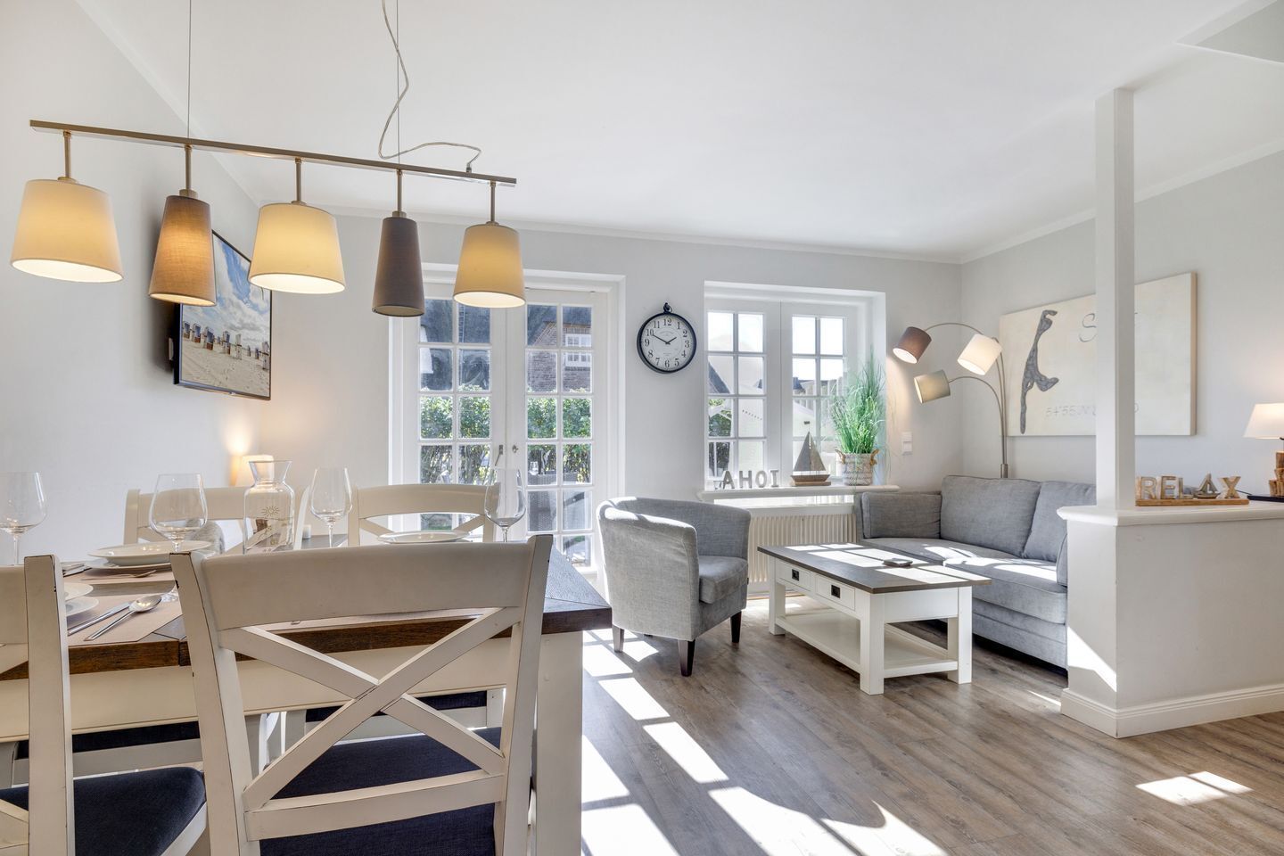 A bright living room with a dining area, large windows, and a modern chandelier.