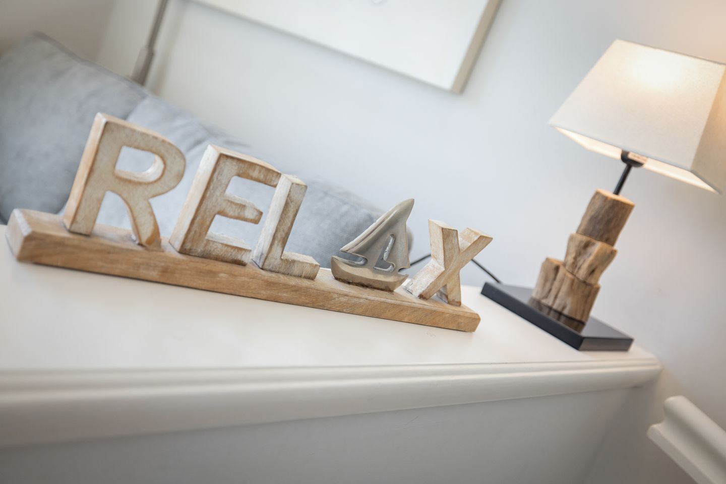 A bed with a white headboard, a wooden block with the word "RELAX" on it, a lamp, and a blue pillow.