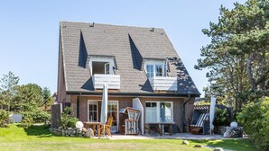 A two-story house with a sloped roof, a small balcony, and a front porch with outdoor furniture.