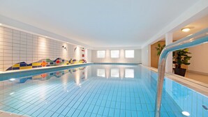 An indoor swimming pool with blue tiles, a tiled wall with colorful patterns, and a wooden door.