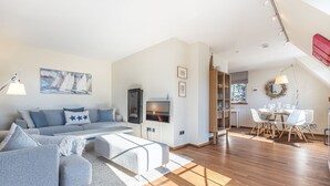 A modern living room with a sofa, a coffee table, and a TV. There is a dining area with a table and chairs.