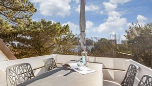 A table set with a glass of water, a bottle, and a menu on a balcony with metal chairs and a view of trees and buildings.