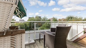Een balkon met rieten meubilair en uitzicht op groen en gebouwen.