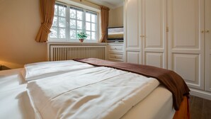 Een hotelkamer met twee bedden, een groot raam met gordijnen, een radiator, een televisie en een kledingkast.