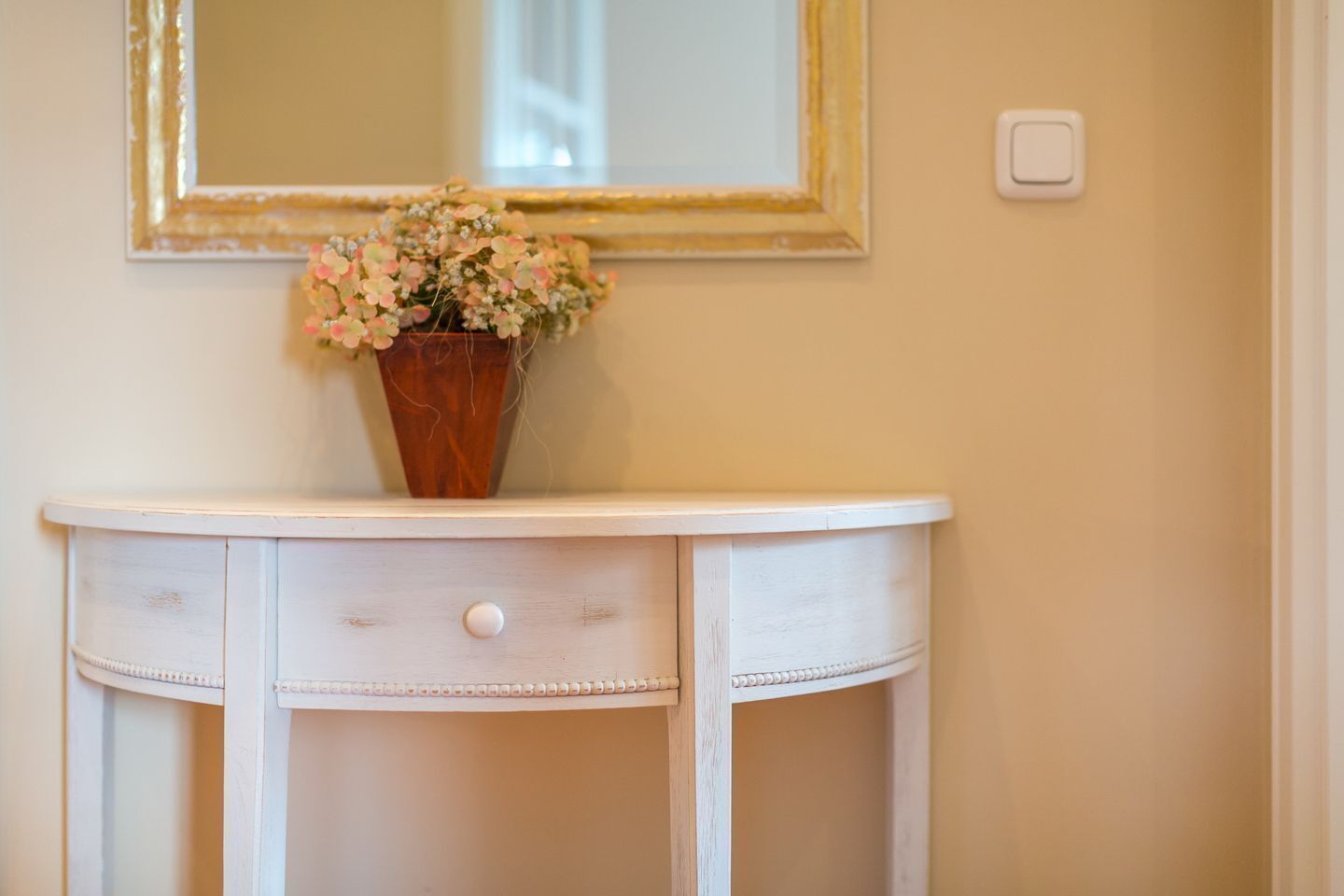 Une coiffeuse blanche avec un seul tiroir et un vase de fleurs posé dessus.