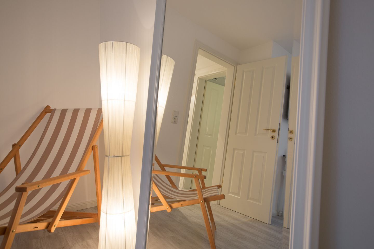 Un couloir avec une chaise en bois et une lampe, qui mène à une porte.