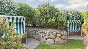 Ein Garten mit einer Steinmauer, zwei gestreiften Stühlen und verschiedenen Pflanzen.
