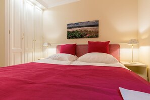 Un dormitorio con una cama grande, dos almohadas rojas, un cabecero blanco y un cuadro de una playa en la pared.