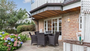Eine Terrasse mit Korbmöbeln, einer Ziegelwand und einem gepflasterten Weg.