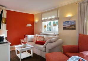 Un salón con una pared de acento roja, un sofá blanco, un sillón rojo y una mesita blanca.