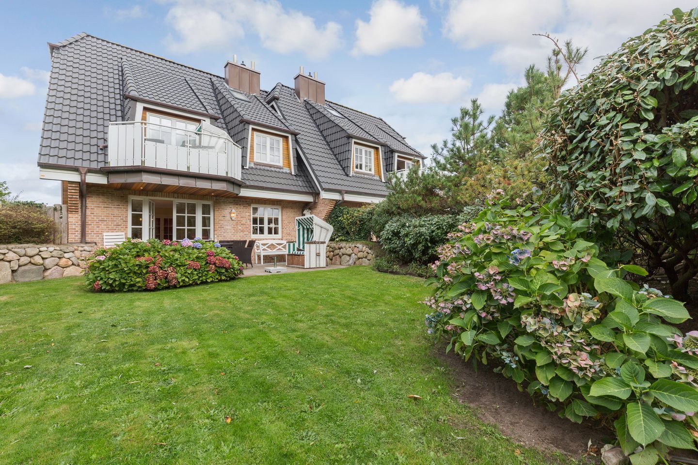 A two-story house with a sloped roof, a stone wall, and a well-maintained lawn.