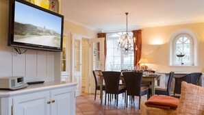 A well-lit living room with a television, a dining area with chairs and a table, and a cozy seating area with a sofa. - Klingler's Hüs, App. 1 - Style Meets Fashion. Bestlage Zwischen Dünen und Dorfteich (Wenningstedt-Braderup (Sylt))