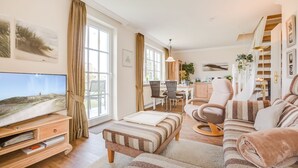 Een ruime woonkamer met een grote televisie, een bank, een eethoek en een trap.