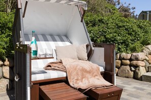 A convertible sofa bed with a striped cushion, a bottle of water, and glasses on a shelf. - Haus am Meer, Strandmuschel - Unmittelbar am Strand Gelegenes, Sehr Großzügiges 3-raum-appartement (Wenningstedt-Braderup (Sylt))