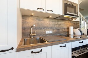 A modern kitchen with a stainless steel sink, a built-in oven, and a microwave. - Haus am Meer, Strandmuschel - Unmittelbar am Strand Gelegenes, Sehr Großzügiges 3-raum-appartement (Wenningstedt-Braderup (Sylt))