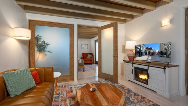 Una sala de estar con sofá de cuero, una mesa de centro de madera, chimenea, televisor y un pasillo que lleva a otra habitación.