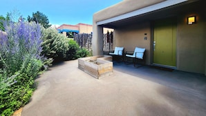 Un patio con una jardinera de madera, dos sillas blancas con cojines y una puerta verde.