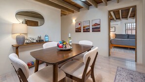 Un comedor con una mesa de madera, sillas blancas, un espejo y obras de arte en la pared.