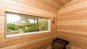 Una sala de sauna con paredes de madera, una ventana con vista a un edificio tradicional y un estante con objetos.