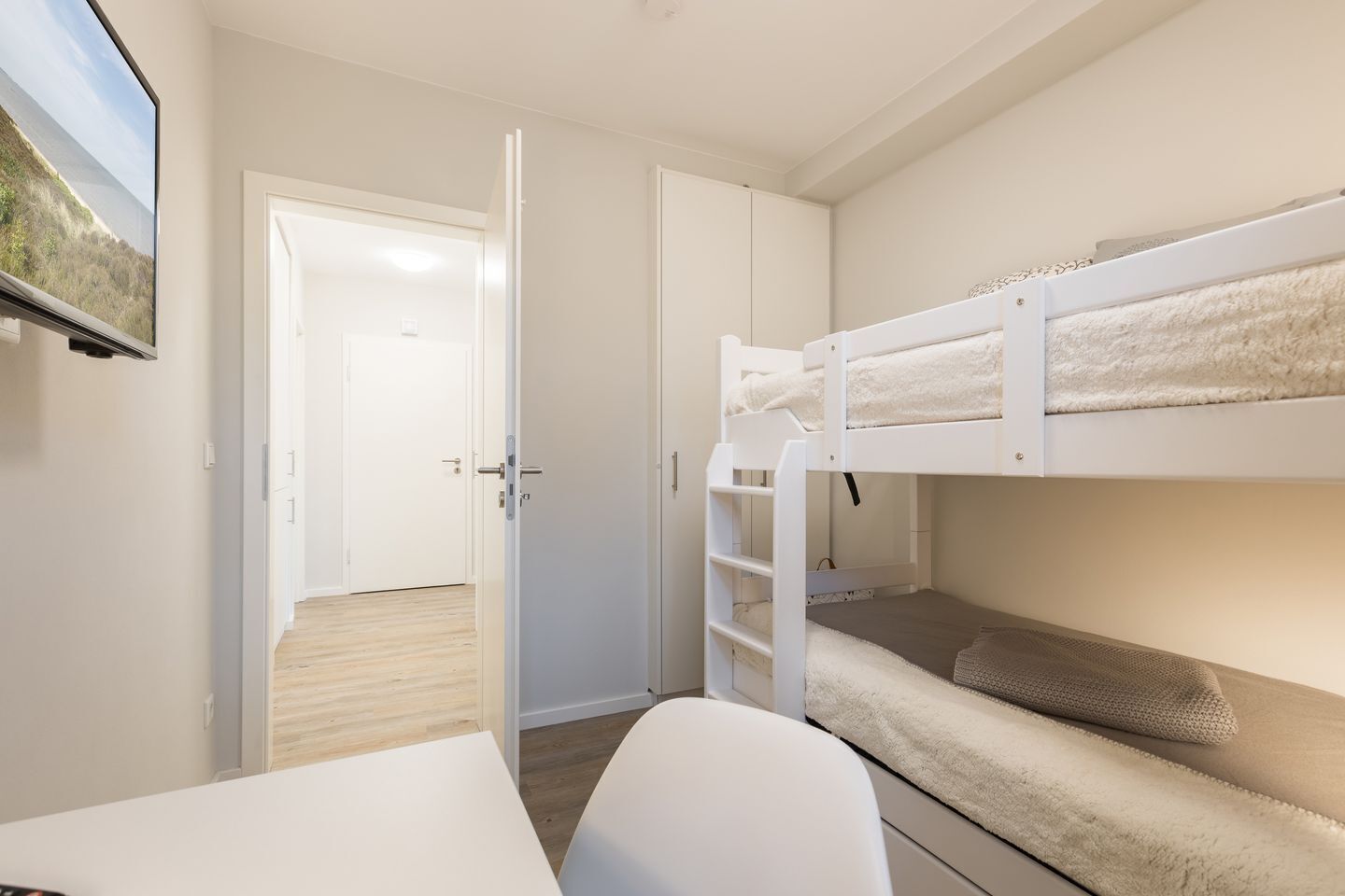 Habitación con literas, un escritorio y una puerta que da a otra habitación.