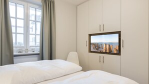 Habitación de hotel con dos camas, un ventanal con cortinas, un armario con televisor y vista al mar.