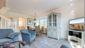 A spacious living room with a dining area, a staircase, and a television on a stand. - Meeresbrise, App. 1 - Feines Wohnen mit Viel Platz Unter Kuscheligem Reet in Bestlage (Wenningstedt-Braderup (Sylt))