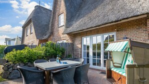 A patio with a table and chairs, a wicker sofa, and a thatched-roof building. - Meeresbrise, App. 1 - Feines Wohnen mit Viel Platz Unter Kuscheligem Reet in Bestlage (Wenningstedt-Braderup (Sylt))