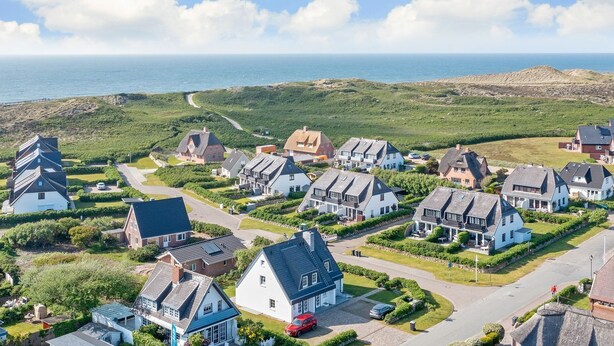 A coastal residential area with houses, a road, and a view of the sea. - Meeresbrise, App. 1 - Feines Wohnen mit Viel Platz Unter Kuscheligem Reet in Bestlage (Wenningstedt-Braderup (Sylt))