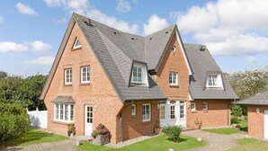 A two-story brick house with a steeply pitched roof, a front porch, and a well-maintained lawn.
