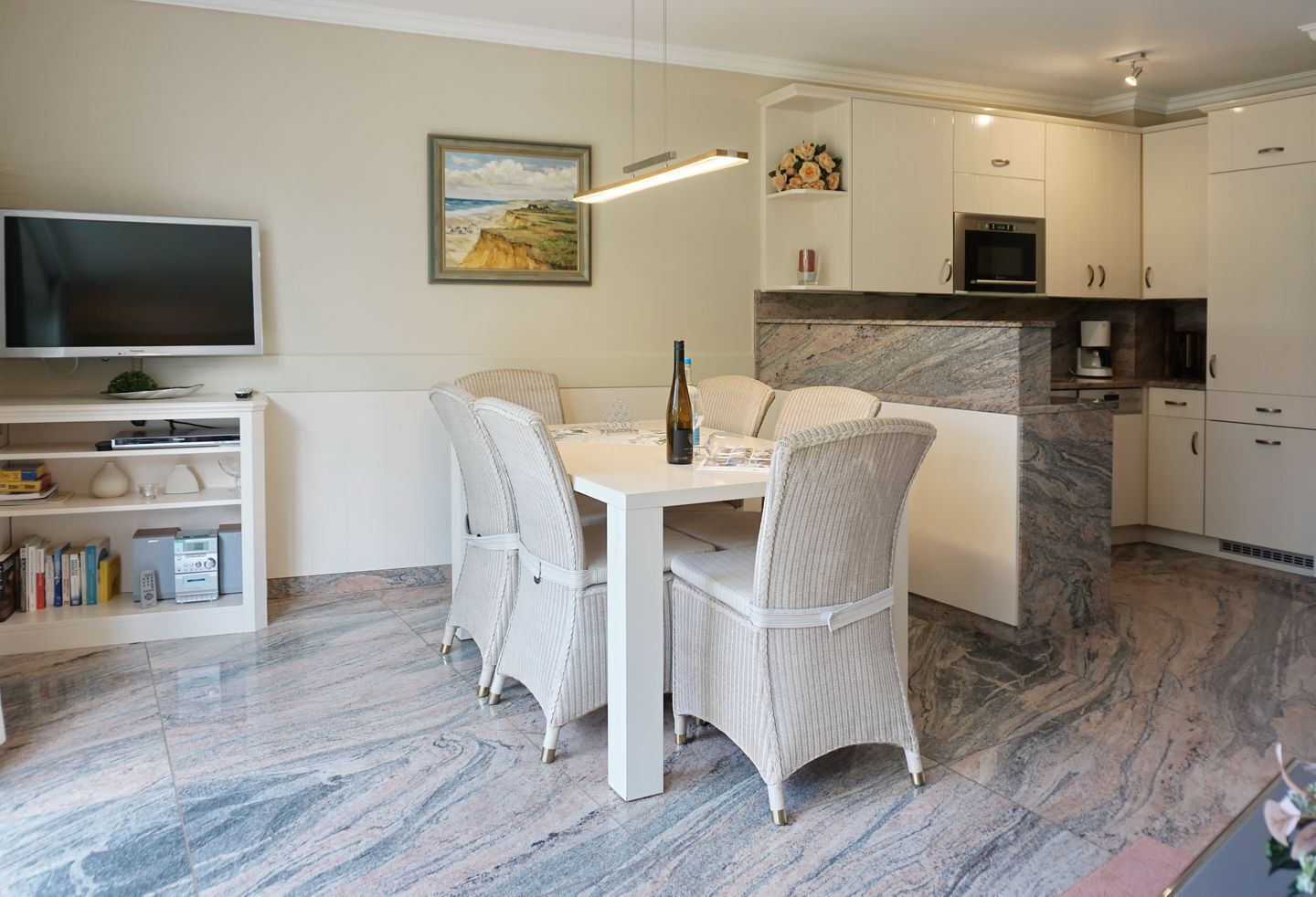 Una cucina moderna con mobili bianchi, un piano di lavoro in marmo e un'area pranzo con sedie in vimini.