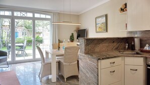 A modern kitchen with a marble countertop, a dining area with wicker chairs, and a large window with a view of the outdoors.
