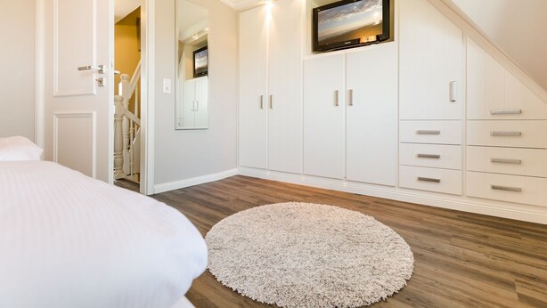 A bedroom with a bed, a round rug, a TV mounted on the wall, and a wardrobe with drawers and doors.