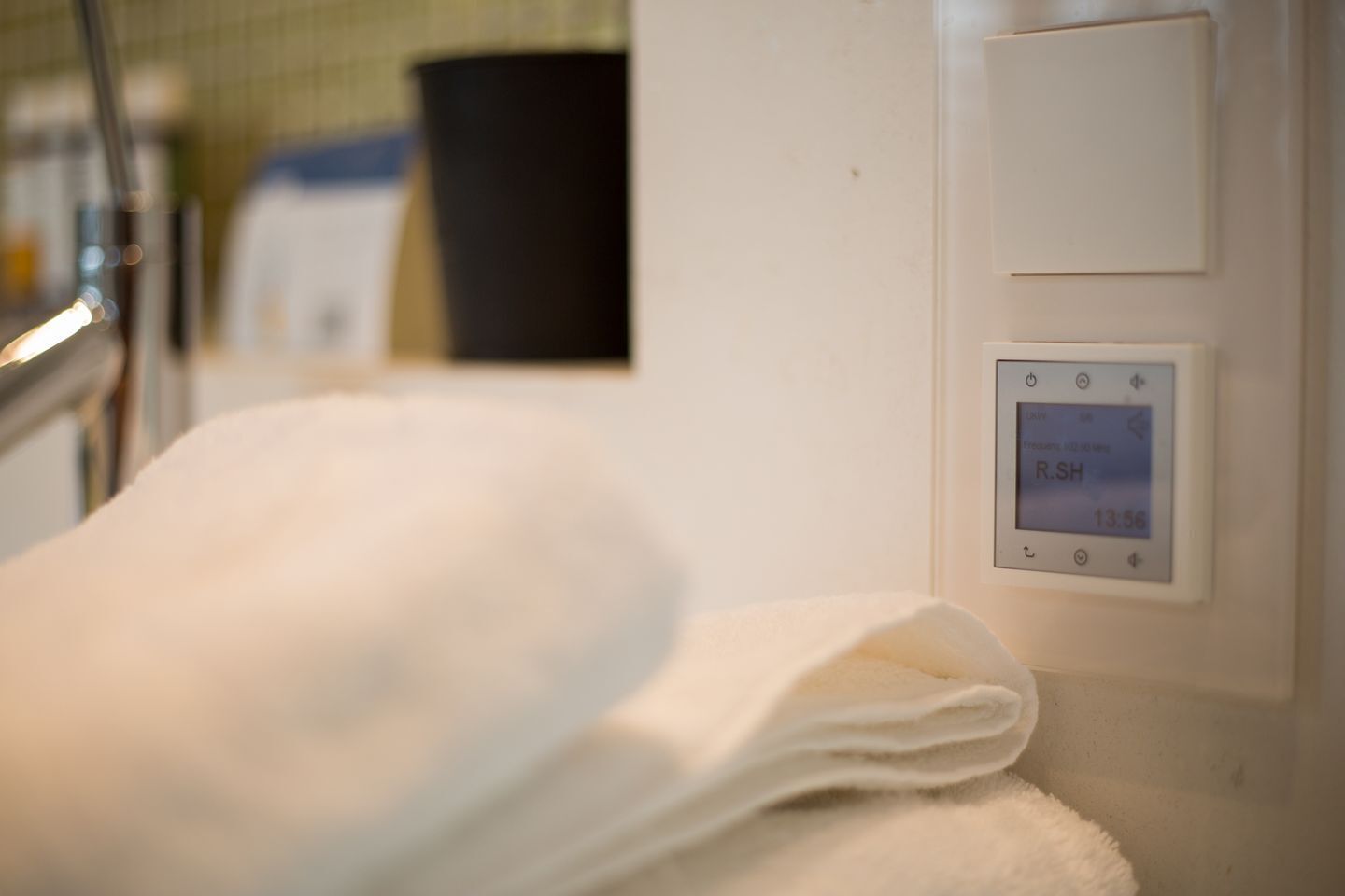 A bathroom with a white towel on a rack, a digital thermostat, and a trash bin.