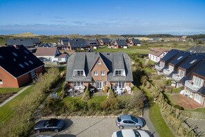 A large house with a spacious front yard, multiple cars parked in the driveway, and a hilly landscape in the background. - Achter Dünem, App. 6 - Achter Dünem - Zwischen Dorfteich & Dünen Sylt at its Best (Wenningstedt-Braderup (Sylt))