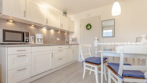 A modern kitchen with white cabinets, a microwave, and a coffee maker. There is a dining table with chairs and a hanging light fixture.