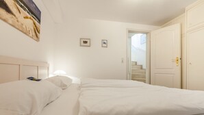 A hotel room with a bed, a nightstand, a lamp, two framed pictures on the wall, and a door leading to a staircase.