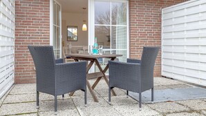 An outdoor patio with two wicker chairs and a table, a bottle of water, and a glass on the table.