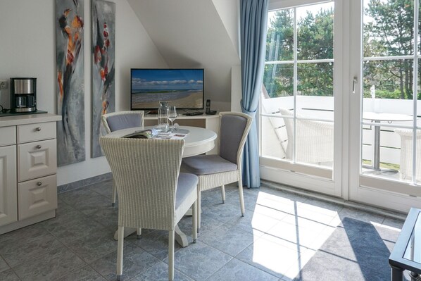A modern room with a dining table, chairs, a coffee machine, artwork, and a large window with a view.