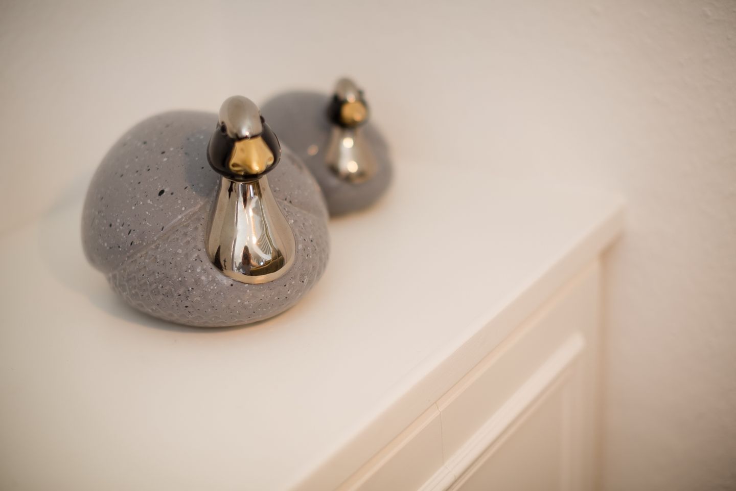 A bathroom with a white sink and two metallic, bird-shaped soap dispensers on a speckled stone countertop.