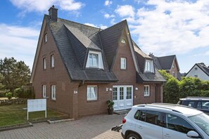 Une maison à deux étages, dotée d’un toit à forte pente, d’une façade en briques et d’une porte blanche. On y trouve une allée menant à une voiture garée devant la maison.