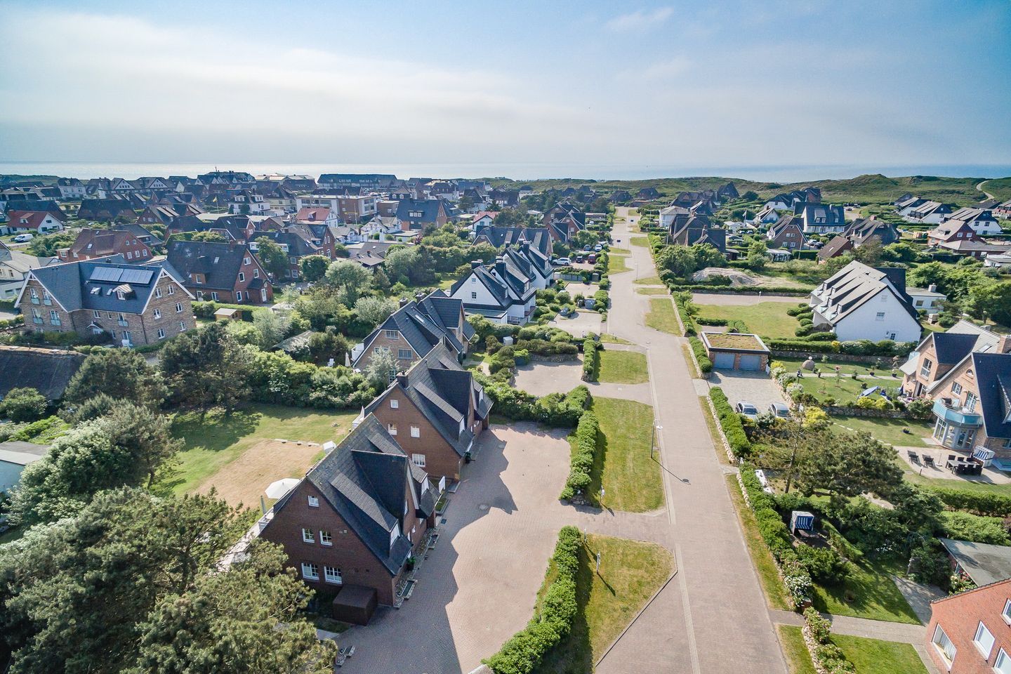 An aerial view of a residential area with houses, green spaces, and a clear sky.