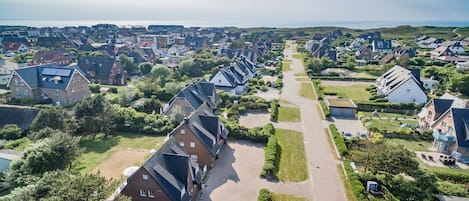 An aerial view of a residential area with houses, green spaces, and a clear sky.