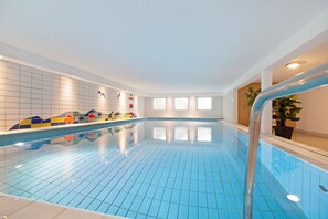 An indoor swimming pool with blue tiles, a tiled wall with colorful patterns, and a wooden door.