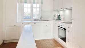 A kitchen with white cabinets, a long countertop, a window with a striped blind, and a coffee maker.