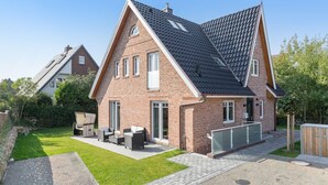 A two-story house with a sloped roof, brick exterior, and a small front yard with outdoor furniture. - Wohnen und Meer, App. 2 - Ein Wohntraum & Viel Mehr, Nahe dem Meer (Sylt)