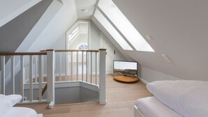A modern loft bedroom with a skylight, wooden staircase, and a flat-screen TV. - Wohnen und Meer, App. 2 - Ein Wohntraum & Viel Mehr, Nahe dem Meer (Sylt)