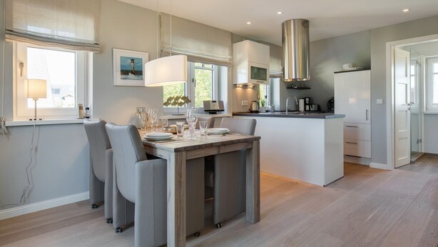 A modern kitchen with a central island, built-in appliances, and a dining area with a table and chairs. - Wohnen und Meer, App. 2 - Ein Wohntraum & Viel Mehr, Nahe dem Meer (Sylt)
