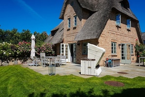 A traditional brick house with a thatched roof, a patio with outdoor furniture, and a garden with flowering plants.