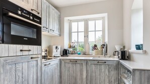 A kitchen with wooden cabinets, a Siemens oven, a coffee maker, and a window with a view of greenery.