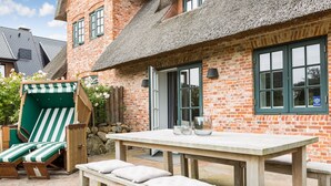 A brick building with a thatched roof, a wooden table with benches, and a green-striped lounge chair. - Watthüs Wenningstedt - Wenningstedter Superlativ (Wenningstedt-Braderup (Sylt))